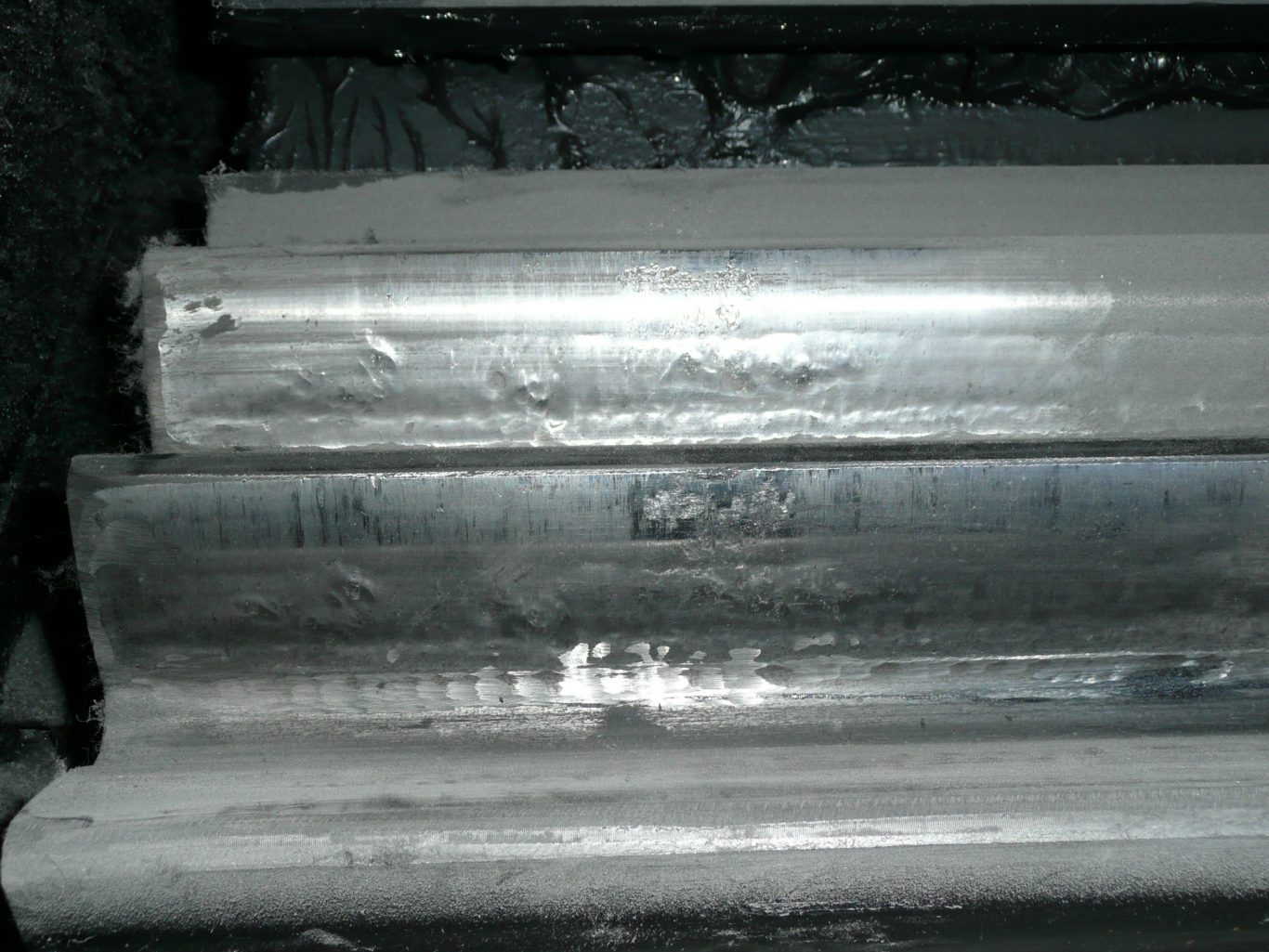 Pinion spur gear with a matt grey surface finish and severe abrasive wear. The teeth in the background are still covered in the lubricant.